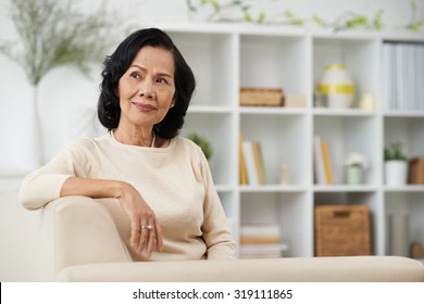 Pensive Vietnamese mature woman sitting on the sofa at home