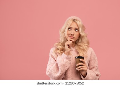 Pensive woman holding takeaway coffee and pondering on offer, looking aside at empty space and touching chin, posing on pink studio background. Unusual offer, making right choice.