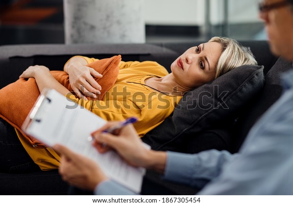 Pensive woman hugging a\
pillow and thinking of something while lying down on the\
psychiatrist\'s couch.