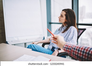 Pensive Woman Looking At Publicity Area Of Board Sitting At Desktop With Male Colleague Pointing,cropped Image Of Man's Hand Showing Mock Up On Flip Chart While Female Employee Looking At It