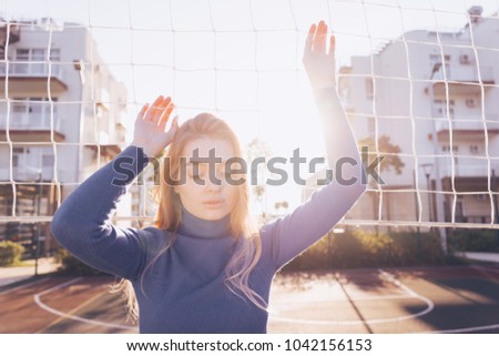 pensive woman posing against the backdrop of a volleyball grid on a sunny day