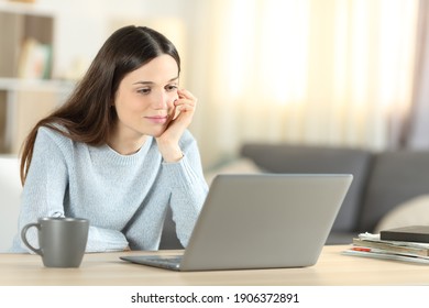 Pensive woman using laptop watching media content sitting at home