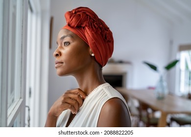 Pensive woman wearing headscarf looking outside window in contemplation. Mature black woman wearing a traditional turban and thinking near window at home. Worried african mature woman with cancer. - Shutterstock ID 2088822205