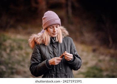 Pensive Woman in Winter Attire Holding a Leaf in the Forest - Powered by Shutterstock