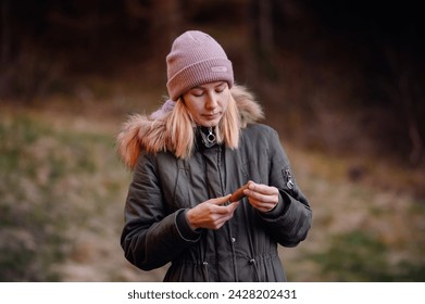 Pensive Woman in Winter Attire Holding a Leaf in the Forest - Powered by Shutterstock