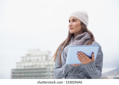 Pensive Woman With Winter Clothes On Using Her Tablet Outdoors On A Cold Grey Day