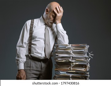 Pensive worried businessman leaning on a pile of paperwork, bureaucracy and administration concept