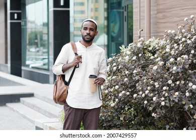 Pensive Young African American Man In Kufi Cap Carrying Satchel And Drinking Coffee On Move