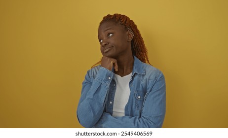 Pensive young african american woman with braided hair wearing a denim jacket over an isolated yellow background - Powered by Shutterstock