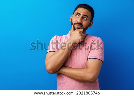 Pensive young arab man thinking and looking up against blue background