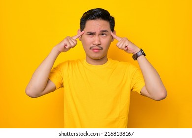 Pensive Young Asian Man In Casual T-shirt Looking Away Trying To Remember Something Isolated On Yellow Background. People Lifestyle Concept
