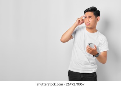 Pensive Young Asian Man With A Serious Face Thinking About A Question, Using A Mobile Phone Isolated On White Background