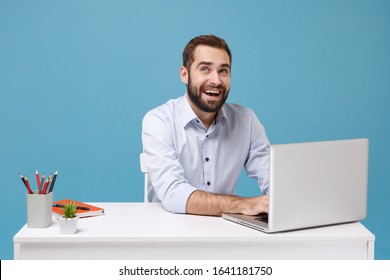 Pensive Young Bearded Man In Light Shirt Sit At White Desk Isolated On Pastel Blue Wall Background. Achievement Business Career Concept. Mock Up Copy Space. Working On Project With Laptop Pc Computer