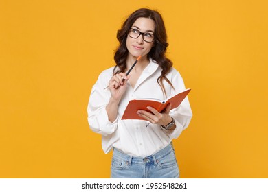 Pensive Young Brunette Business Woman In White Shirt Glasses Isolated On Yellow Background Studio Portrait. Achievement Career Wealth Business Concept. Mock Up Copy Space. Writing Notes In Notebook