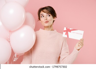 Pensive young brunette woman in knitted casual sweater posing isolated on pastel pink background. Birthday holiday party people emotions concept. Celebrating hold air balloons gift certificate