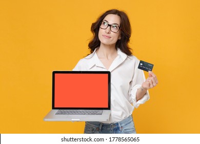 Pensive Young Business Woman In White Shirt Glasses Isolated On Yellow Background Studio. Achievement Career Wealth Business Concept. Hold Laptop Pc Computer With Blank Empty Screen Credit Bank Card