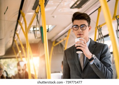 pensive young businessman in eyeglasses drinking coffee to go in bus