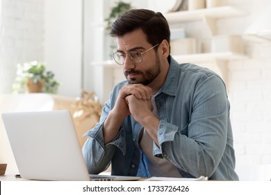 Pensive young Caucasian man in glasses sit at desk look at laptop screen thinking pondering, thoughtful millennial male in spectacles work at computer consider ideas solving problems at home workplace - Shutterstock ID 1733726426