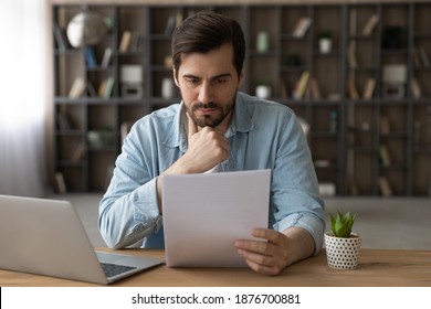 Pensive young Caucasian man sit at desk at home work on laptop read paper document. Thoughtful millennial male distracted from computer job consider post paperwork or letter correspondence news. - Powered by Shutterstock