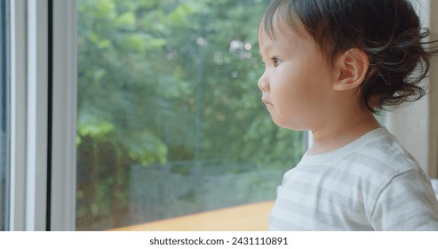 A pensive young child gazes out a window into a lush garden, lost in thought, with soft natural light accentuating a peaceful expression