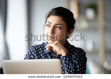 Pensive young ethnic woman distracted from computer work look in window distance thinking, thoughtful millennial Indian girl lost in thoughts pondering solving problem, making decision