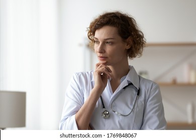 Pensive Young Female Nurse Or GP Wear White Medical Uniform Look In Window Distance Thinking Making Decision, Thoughtful Woman Doctor Lost In Thoughts, Analyze Patient Anamnesis, Healthcare Concept