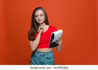 Pensive Young Girl Make Notes In Notepad, Create Ideas For Project, Make Schedule, To Do List On Orange Background