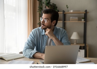 Pensive young guy employee sit at workplace look aside of pc screen think on problem of research project. Thoughtful businessman analyze information ponder chances of success make calculations in mind