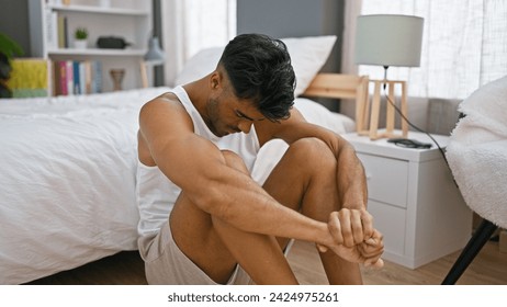 A pensive young hispanic man sits on a bed in a modern bedroom, exuding a sense of contemplation or worry.