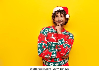 pensive young indian man in new year clothes thinking and planning over yellow isolated background, puzzled hindu guy in santa hat and christmas sweater dreaming and imagining - Powered by Shutterstock