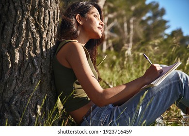 Pensive Young Lady Sitting Outside With A Journal On Her Lap And A Pen In Her Hand