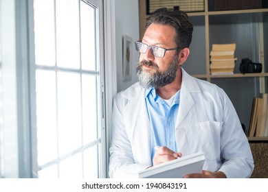Pensive young male caucasian doctor in white medical uniform look in window distance thinking or pondering, serious man GP plan future career or success in medicine, visualize at workplace writing