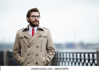 Pensive young man in beige trenchcoat hanging around outdoors