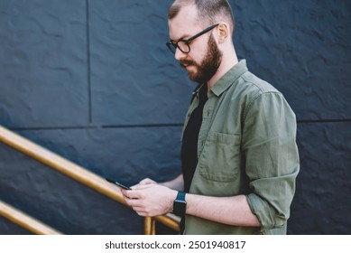 Pensive young man blogger dressed in casual wear updating profile on modern smartphone using 4g internet connection walking outdoors,Hipster guy installing app on cellular going up stairs - Powered by Shutterstock