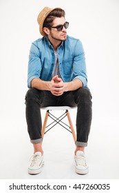 Pensive Young Man In Hat And Sunglasses Sitting On Chair And Thinking Over White Background