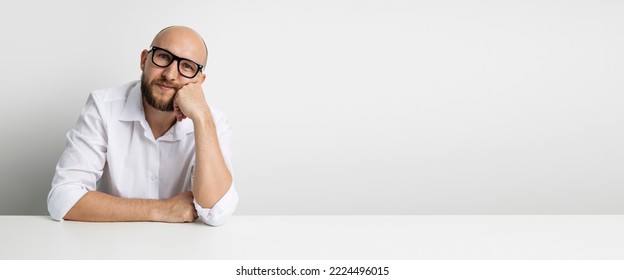 Pensive Young Man Holding Hand Under Chin While Sitting At Table On White Background. Banner.