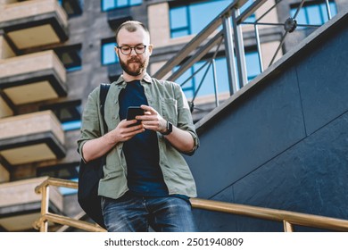 Pensive young man messaging in online chat on modern smartphone device using free 4G internet going down on stairs in urban stairs.Hipster blogger reading notification on mobile phone - Powered by Shutterstock