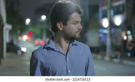 Pensive Young Man Walking In City Street At Night. Thoughtful Person Walks In Urban Sidewalk In Mental Reflection In The Evening