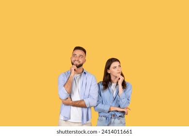 Pensive young man and woman with hands on their chins looking upwards at copy space, deep in thought, suggesting curiosity or decision-making against yellow background - Powered by Shutterstock