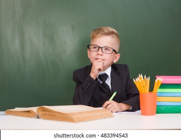 Pensive young student in black suit near empty green chalkboard.