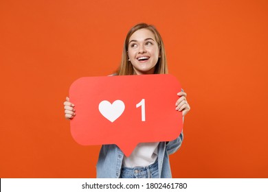 Pensive young woman 20s in casual denim clothes posing isolated on orange wall background. People lifestyle concept. Mock up copy space. Hold huge like sign from social network heart form looking up
