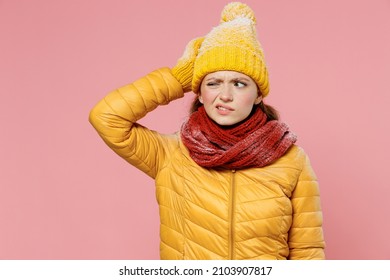 Pensive young woman 20s years old wears yellow jacket hat mittens looking around think put hand on head lost in thought and conjectures isolated on plain pastel light pink background studio portrait