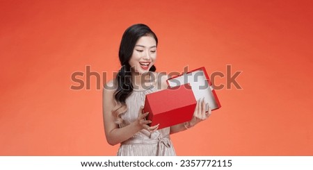 Pensive young woman in evening dress hold present box with gift ribbon bow isolated on red background