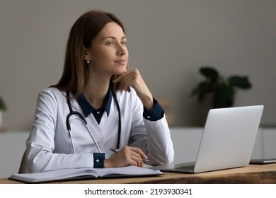 Pensive young woman general practitioner doctor medical worker in white uniform looking in distance, thinking on disease treatment, taking break waiting for next patient in modern clinic office.