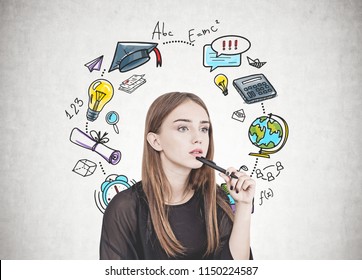 Pensive young woman with long fair hair holding a pen near her chin. A concrete wall background with an education sketch on it.