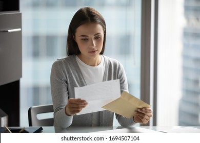 Pensive young woman sit at desk in office open envelope read post correspondence, focused thoughtful millennial female get postal letter consider offer or suggestion, promotion or dismissal notice