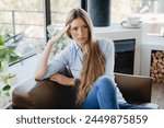 Pensive young woman sitting in the armchair thinking about sad problems issues at home. Depressed female lady girl having period crumps, nostalgy, relationship breakup