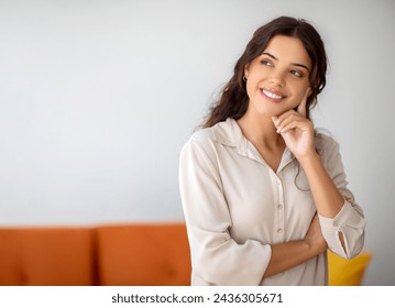 Pensive young woman smiling gently and looking away at copy space, happy female lost in thought daydreaming at home, planning or thinking about something, standing in living room interior - Powered by Shutterstock