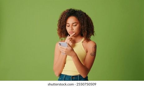 Pensive young woman using smartphone at green screen background, scrolling and thinking - Powered by Shutterstock