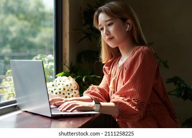 Pensive Young Woman Working On Laptop At Window Sill In Coffeeshop